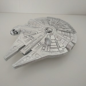 May include: A white model of the Millennium Falcon spaceship from Star Wars. The model is detailed and has a realistic appearance.