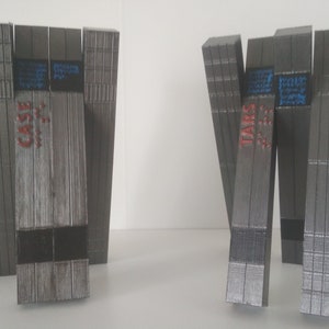 May include: Two wooden structures, each made of stacked wooden planks, with the words "CASE" and "TARS" printed on them in red. The structures are gray and have a wood grain texture.