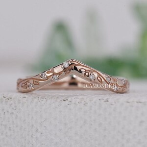Könnte beinhalten: Roségoldener Chevron-Ring mit Blatt- und Weinranken-Details, verziert mit kleinen Diamanten. Der Ring hat ein zartes, geschwungenes Design und liegt auf einer strukturierten Oberfläche. Das Wort "DIAMONDIQUE" ist sichtbar.