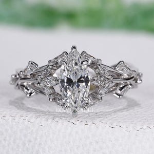 Könnte beinhalten: Ein Verlobungsring mit Diamanten im Marquise-Schliff und ein passendes Band. Der Ring hat einen zentralen Diamanten im Marquise-Schliff, umgeben von kleineren Diamanten in einem floralen Design. Das Band ist ebenfalls mit Diamanten verziert und sorgt für einen funkelnden, eleganten Look.