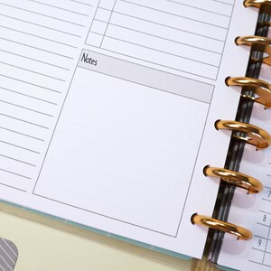 May include: A close-up of a blank page in a planner with the word "Notes" at the top. The planner has gold rings and a white background.