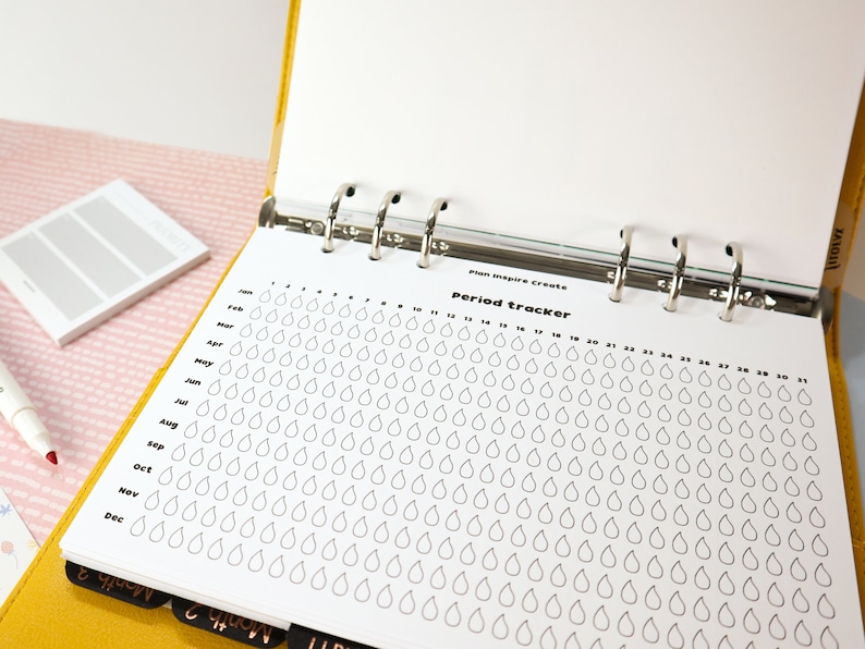 May include: A white page with a period tracker chart. The chart has a column for each month of the year and a row for each day of the month. Each day is represented by a small teardrop shape. The chart is titled "Period Tracker" and is labeled "Plan Inspire Create".