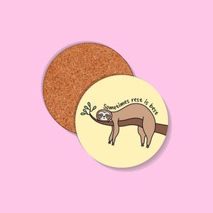 May include: Two round coasters. One is made of cork. The other is yellow with a cartoon sloth on a branch, with the text "Sometimes rest is best".