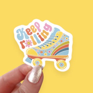 May include: A colorful sticker featuring a retro roller skate design. The skate is yellow, blue, and orange with floral accents and rainbow stripes. The sticker has the words "Keep Rolling" in a playful font.