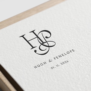 May include: A white card with a black monogram of the letters "H" and "P" in a script font. The text "HUGH & PENELOPE" and "01.11.2026" is printed below the monogram.