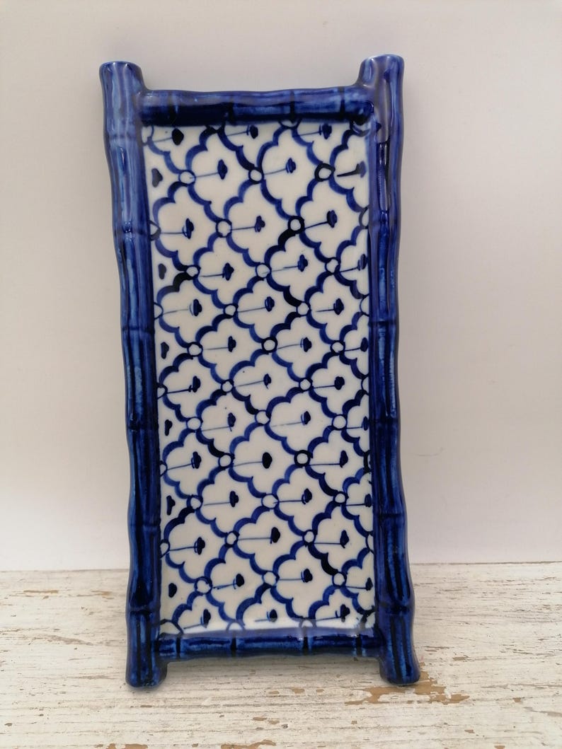 May include: A rectangular ceramic tray with a blue bamboo-style frame and a white and blue floral pattern. The tray has a raised edge and is designed for decorative or functional use. The overall design is reminiscent of traditional Asian pottery.
