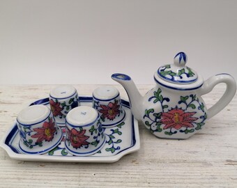Puede incluir: Un juego de té de porcelana blanca con diseños florales azules y rojos. El juego incluye una tetera, cuatro tazas y una bandeja.