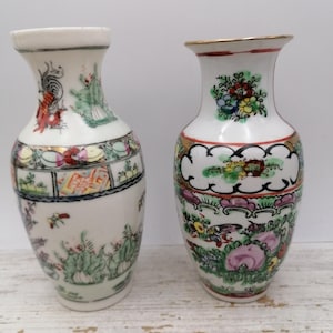 May include: Two white porcelain vases with colorful floral and bird designs. One vase features a rooster, while the other has a gold rim. The vases are decorated with intricate patterns and vibrant colors.
