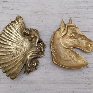 Op de afbeelding: Twee vintage messing sieradenbakjes. Een heeft een gevleugelde figuur met een waaiervormig ontwerp. De andere is een paardenkop.