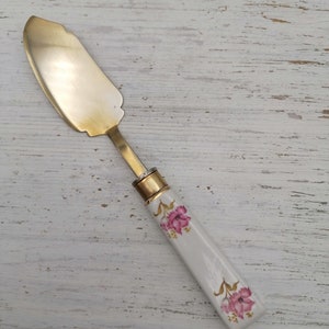 May include: A gold butter knife with a white porcelain handle decorated with pink flowers.