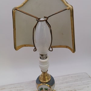 May include: A vintage porcelain table lamp with a white shade and a blue and white base with floral details. The lamp has a gold-tone metal base and a white porcelain light bulb.