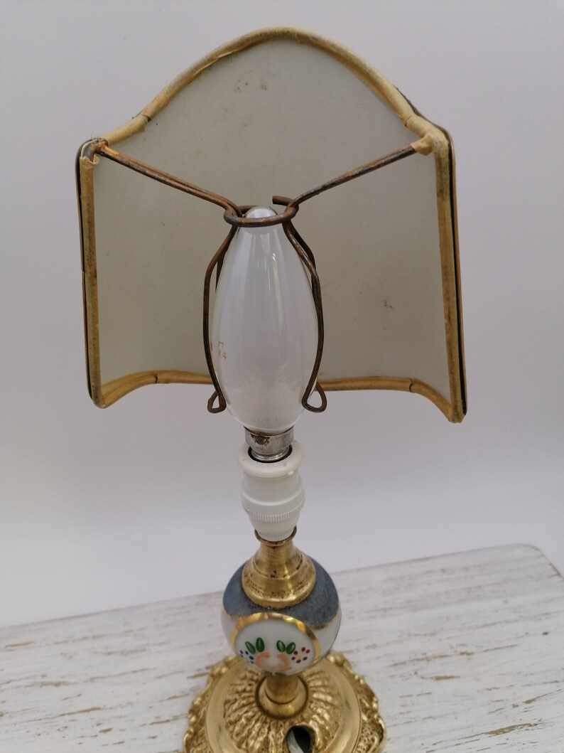 May include: A vintage porcelain table lamp with a white shade and a blue and white base with floral details. The lamp has a gold-tone metal base and a white porcelain light bulb.