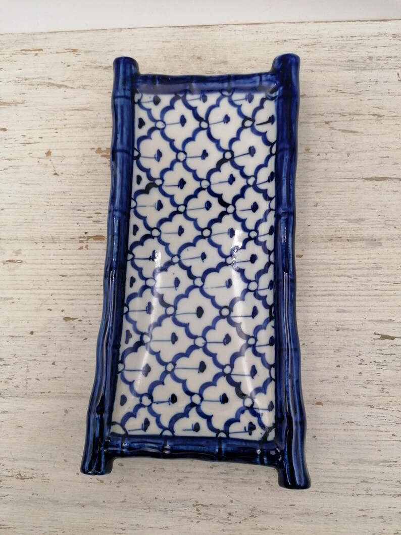 May include: Rectangular ceramic serving dish with a bamboo-style frame in glossy dark blue. The interior features a white background with a repeating blue floral pattern. Ideal for serving appetizers or small dishes.