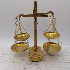 Peut inclure: Une balance ancienne en laiton avec deux ensembles de plateaux ovales suspendus par des chaînes. La balance a une colonne centrale et une base décorative. Le laiton est de couleur dorée.