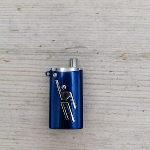 Puede incluir: Un llavero de metal azul con una figura plateada de una persona practicando un deporte. El llavero tiene una parte superior plateada y un anillo plateado.
