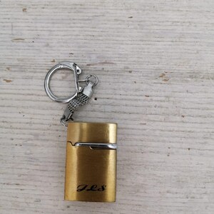 Puede incluir: Un encendedor de llavero de color dorado con una cadena y un anillo plateados. El encendedor tiene la inscripci&oacute;n "J.L.S." en la parte delantera.