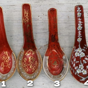 Puede incluir: Cuatro cucharas de sopa de cerámica roja con detalles dorados y diseños intrincados. Cada cuchara presenta un patrón único, incluyendo motivos florales y caracteres chinos. Las cucharas tienen un acabado brillante y un borde dorado.