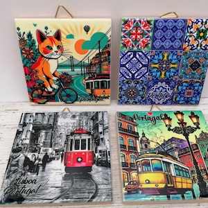 May include: Four decorative ceramic tiles with gold hanging loops. The tiles feature colorful illustrations of Portugal. One tile shows a cat on a bicycle, another has a patchwork design, and two depict city scenes with trams. The word "Portugal" is visible.