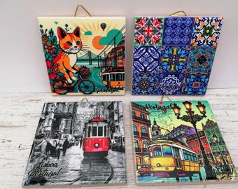 May include: Four decorative ceramic tiles with gold hanging loops. The tiles feature colorful illustrations of Portugal. One tile shows a cat on a bicycle, another has a patchwork design, and two depict city scenes with trams. The word "Portugal" is visible.