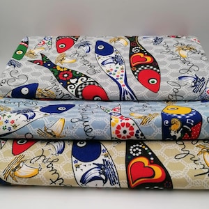 Può includere: Tre pezzi di tessuto piegati con un motivo ripetitivo di pesci stilizzati colorati, piccole barche a vela e il testo in corsivo Sardinha Portugal. Lo sfondo di ogni pezzo di tessuto mostra un disegno a rete simile a una corda bianca.