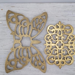May include: Two gold metal decorative coasters. One is shaped like a butterfly and the other is a more ornate design.