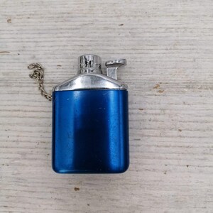 Puede incluir: Un encendedor de metal azul con una parte superior plateada y una cadena adjunta.
