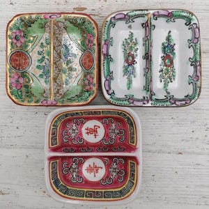 Op de afbeelding: Drie antieke verdeelde serveerschalen. De schalen hebben bloemen- en geometrische ontwerpen in roze, groen, goud en rood. De schalen zijn vierkant met afgeronde hoeken en zijn gemaakt van porselein.