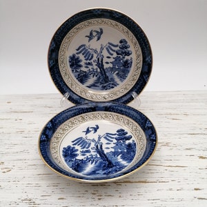 Puede incluir: Dos cuencos de porcelana azul y blanco con borde dorado y diseño de sauce. Los cuencos están apilados uno encima del otro.