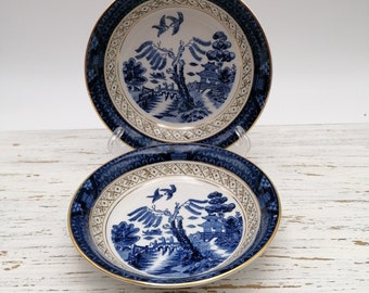 May include: Two blue and white porcelain bowls with a gold rim and a willow pattern design. The bowls are stacked on top of each other.