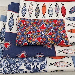 Könnte beinhalten: Ein Stapel dekorativer Stoffquadrate mit Fisch- und Blumenmustern. Die Quadrate weisen eine Vielzahl von Designs auf, darunter Fische mit Herzen, Blumenmuster und blau-weiße Fliesenmotive. Die Farbpalette umfasst Blau, Rot, Orange und Weiß.