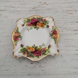 Pode incluir: Um cinzeiro de cerâmica branca com uma borda dourada e um design floral com rosas vermelhas, amarelas e verdes.
