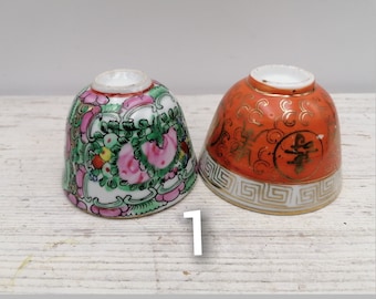 May include: Two small ceramic teacups with intricate designs. One cup is white with pink and green floral patterns, the other is orange with gold accents and Chinese characters.