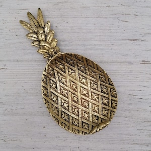 May include: A gold pineapple-shaped dish with a detailed, woven pattern. The dish is made of metal and has a raised, leafy top.