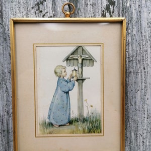 Può includere: Un'illustrazione incorniciata di un bambino piccolo che tiene una lanterna e prega davanti a una croce di legno con una figura di Gesù sopra. L'illustrazione è su uno sfondo di erba verde e fiori.