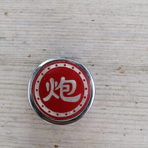 Puede incluir: Un bot&oacute;n redondo plateado y rojo con el car&aacute;cter chino para "fuego" en blanco sobre fondo rojo. El bot&oacute;n tiene un borde blanco punteado.