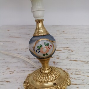 May include: A gold table lamp with a white and blue glass shade featuring a floral design. The lamp has a decorative base with a scalloped edge.