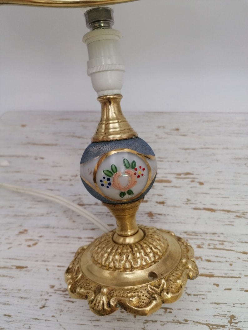 May include: A gold table lamp with a white and blue glass shade featuring a floral design. The lamp has a decorative base with a scalloped edge.