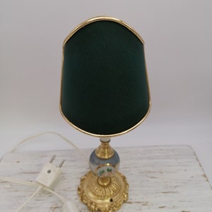 May include: A small table lamp with a green fabric shade and a gold base. The base is decorated with a floral design.