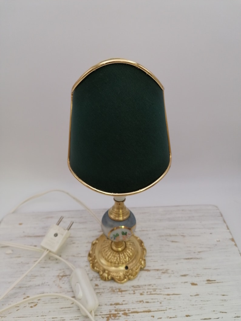 May include: A small table lamp with a green fabric shade and a gold base. The base is decorated with a floral design.