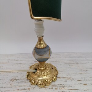 May include: A vintage table lamp with a green fabric shade and a gold base. The base is decorated with a white and blue mosaic pattern.