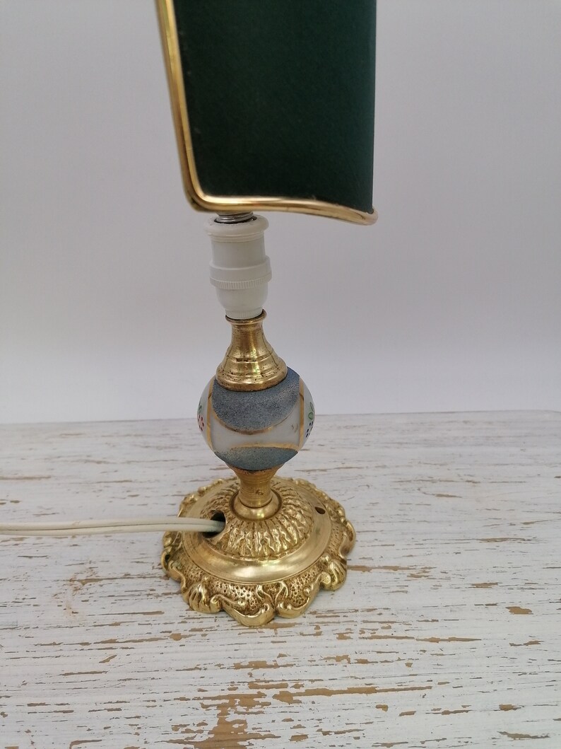 May include: A vintage table lamp with a green fabric shade and a gold base. The base is decorated with a white and blue mosaic pattern.