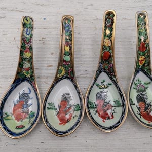 May include: Four small porcelain spoons with gold trim and colourful rooster designs. The spoons have a traditional Chinese style.