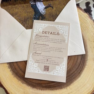 Könnte beinhalten: Eine braune Karte mit weißen dekorativen Rändern und dem Wort "DETAILS" in brauner Schrift. Die Karte enthält Informationen über Transport, Unterkunft und Ankunft für eine Hochzeit. Ein QR-Code ist am unteren Rand der Karte enthalten.