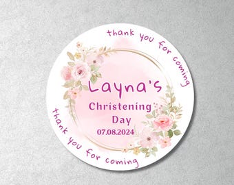 May include: A round sticker with a floral design and the text "Layna's Christening Day 07.08.2024". The sticker has a pink watercolor background and a gold border. The words "thank you for coming" are written around the edge.