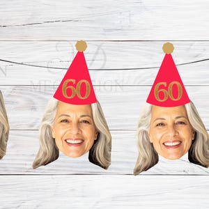 May include: A banner with four cutouts of a smiling woman with grey hair. Each cutout wears a red party hat with a gold "60" on it. The hats have gold pom-poms. The banner is strung on a white string against a white wood background.