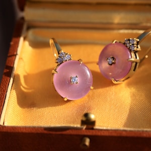 Könnte beinhalten: Ein Paar goldene Ohrringe mit rosafarbenem Stein und Diamantbesatz. Die Ohrringe befinden sich in einer kleinen braunen Schachtel mit gelber Auskleidung.