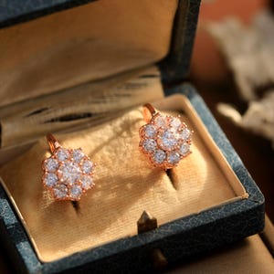 Puede incluir: Un par de pendientes de oro rosa con un racimo de piedras redondas transparentes en forma de flor, presentados en una caja de joyer&iacute;a de terciopelo azul.