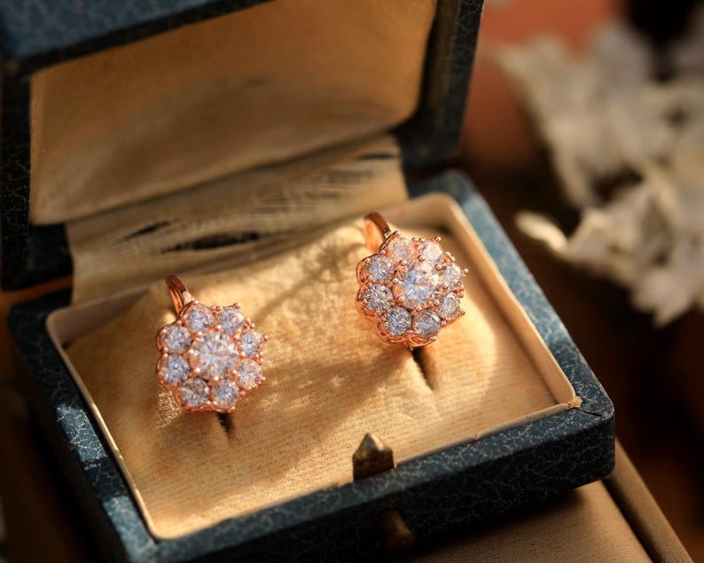 Puede incluir: Un par de pendientes de oro rosa con un racimo de piedras redondas transparentes en forma de flor, presentados en una caja de joyer&iacute;a de terciopelo azul.