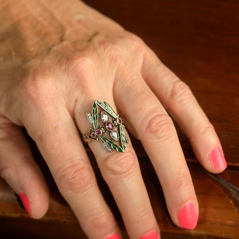 Pode incluir: Um anel de ouro com um design de esmalte verde que apresenta uma lib&eacute;lula com detalhes em rubi e diamante.