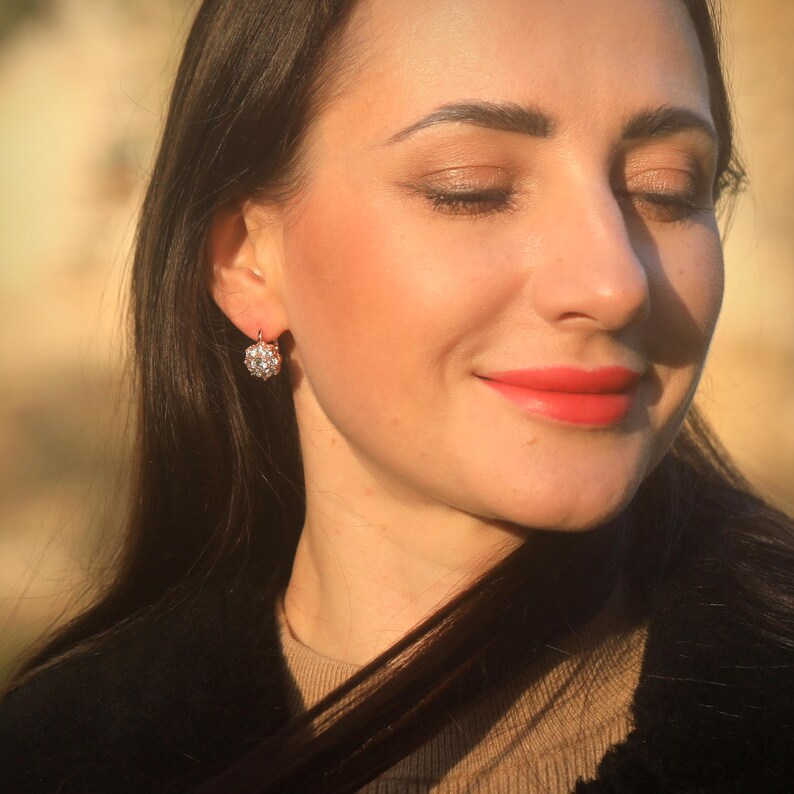 Puede incluir: Primer plano de la cara de una mujer con los ojos cerrados. Lleva un par de peque&ntilde;os pendientes redondos con piedras transparentes.